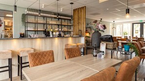 Un restaurant moderne doté d’un bar, de meubles en bois et d’une grande fenêtre laissant entrer la lumière naturelle.