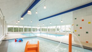 Une piscine intérieure avec un toboggan, un espace de jeux aquatiques et une vue sur la verdure environnante.