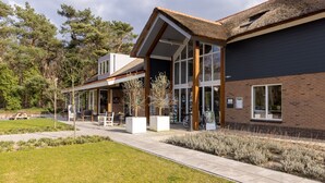 Un bâtiment moderne doté de grandes fenêtres, d’un espace extérieur aménagé avec une terrasse couverte et d’une pelouse bien entretenue.
