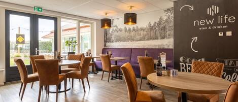 A modern restaurant interior with wooden flooring, round tables, and cushioned chairs. There is a large mural on the wall and a sign that reads "new life".