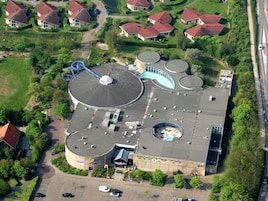 Vue aérienne d’un bâtiment doté de nombreuses structures cylindriques, d’un grand dôme circulaire et d’une zone de stationnement.