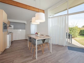 A modern kitchen with wooden flooring, white cabinets, and a dining area with a table and chairs.