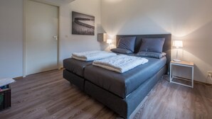 Un dormitorio con cama, lámparas de noche, un cuadro y suelo de madera.
