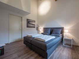 A bedroom with a bed, bedside lamps, a painting, and a wooden floor.