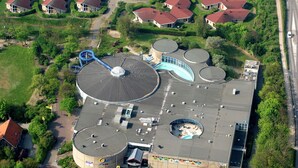 Vista aerea di un edificio con diverse strutture cilindriche, un'ampia cupola circolare e un'area di parcheggio.