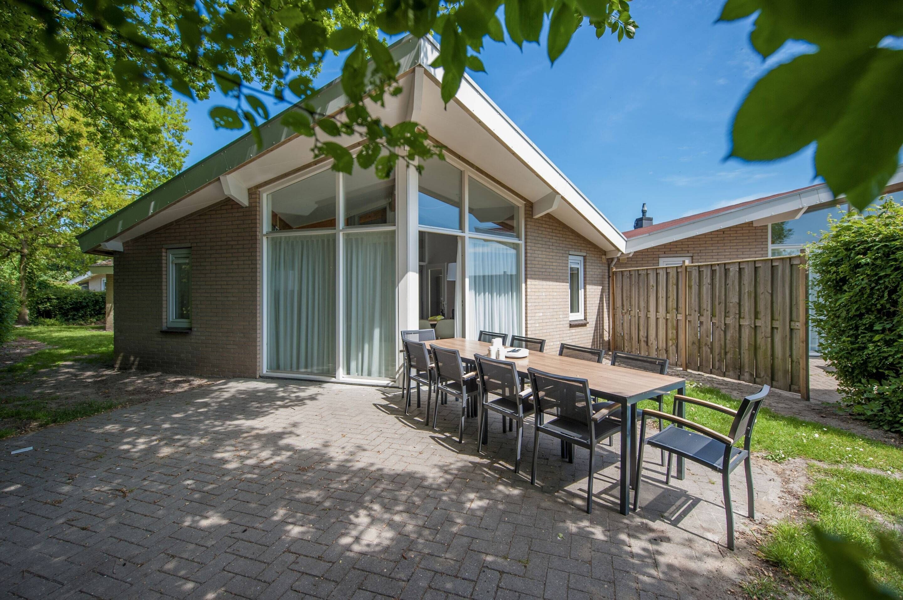 Et hus med en terrasse, et spisebord med stole og et træhegn.