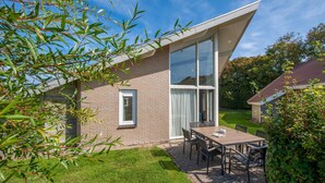 Ein modernes Haus mit großen Glasfenstern, einer Ziegel Fassade und einer Terrasse mit Tisch und Stühlen.