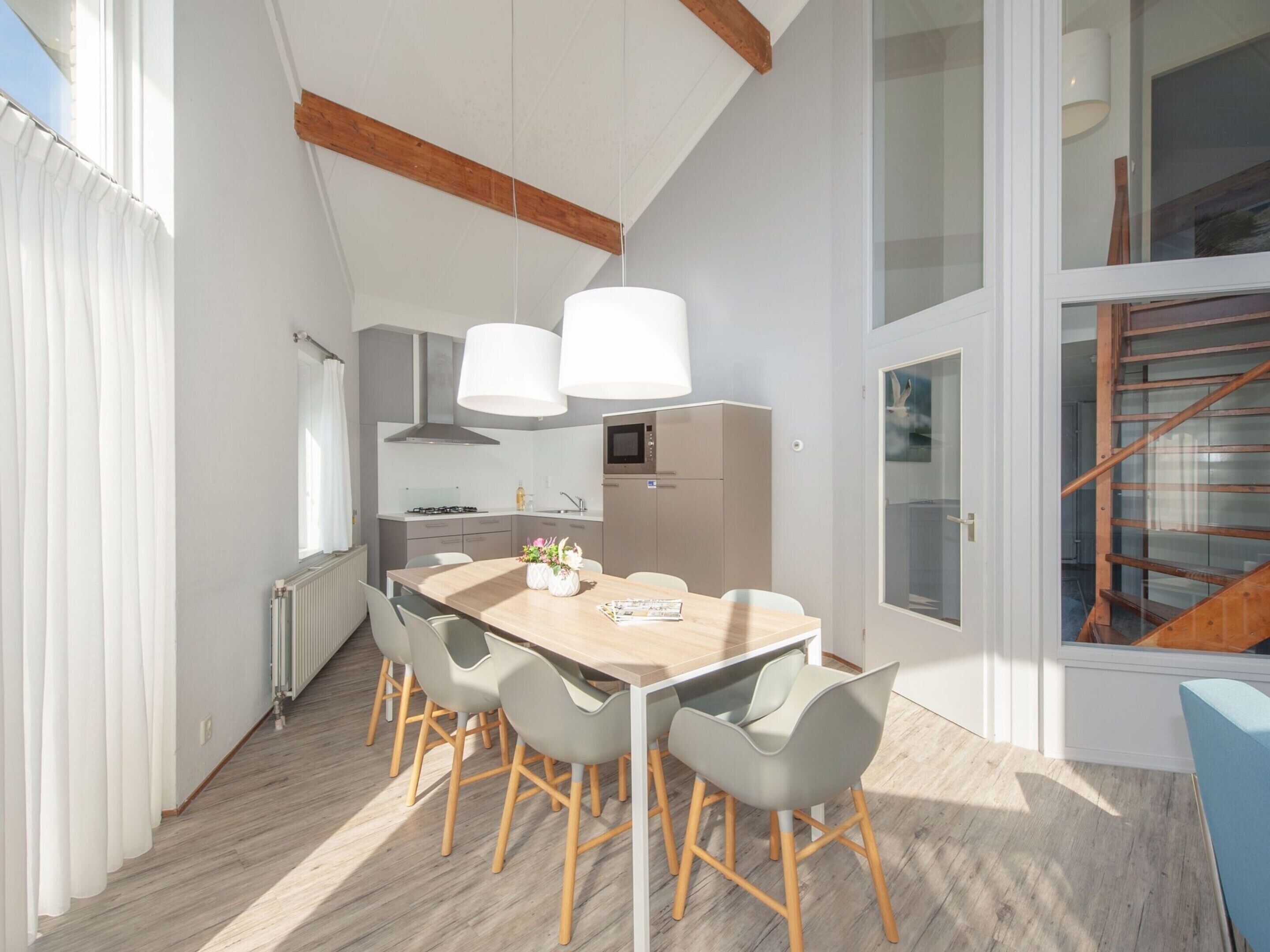 Une cuisine moderne avec un coin repas, comprenant une table en bois, des chaises grises et des luminaires suspendus.