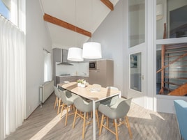 A modern kitchen with a dining area, featuring a wooden table, grey chairs, and pendant lights.