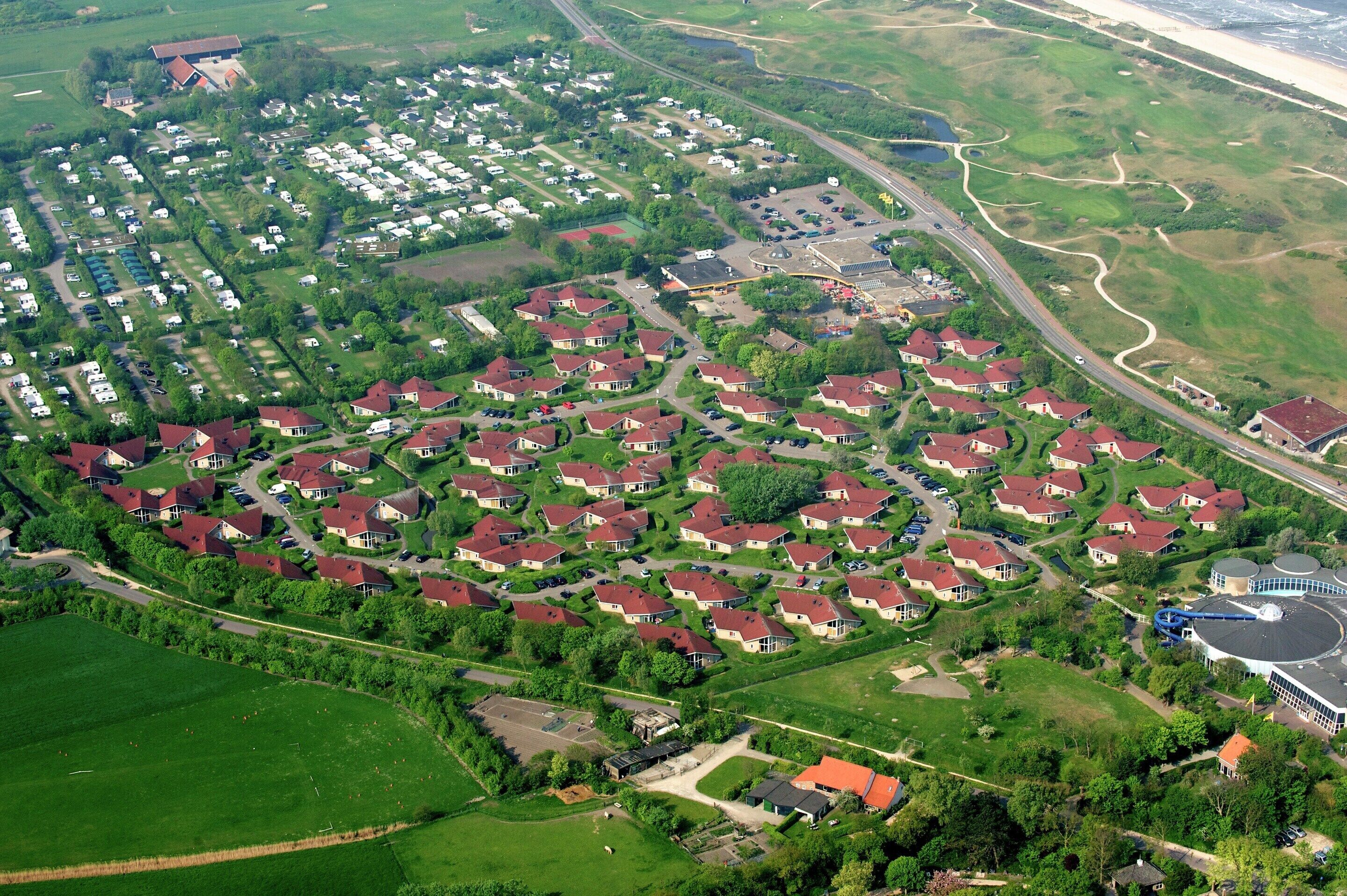 Luchtbeeld van een woongebied met meerdere huizen, wegen en groene ruimtes.