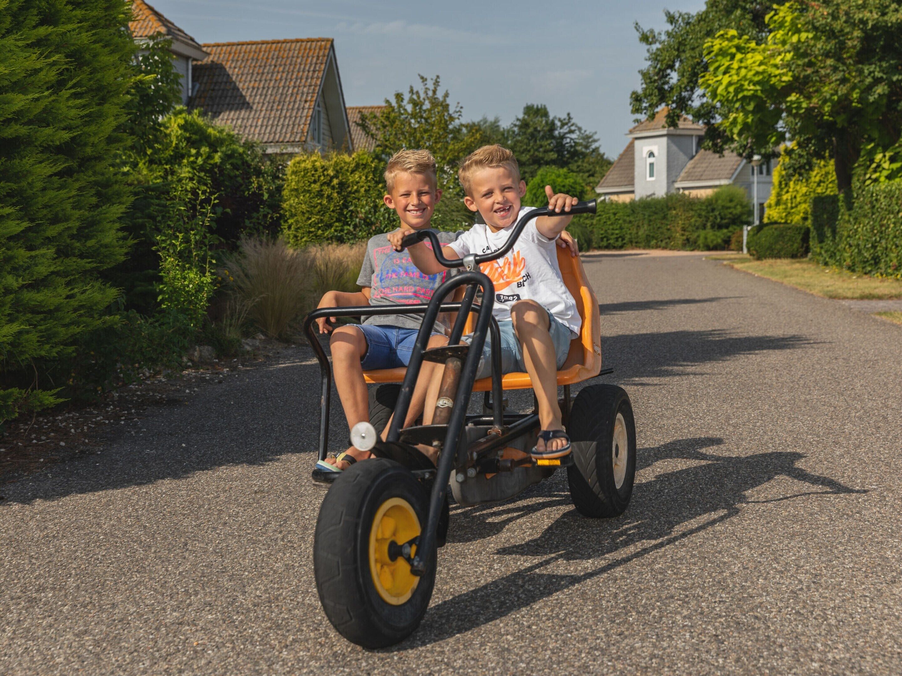 Two children in a small, open-front vehicle on a residential street.