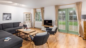 A modern living room with a sectional sofa, a coffee table, and two armchairs. There is a television, a cabinet, and a window with curtains. - Villa in Banjaard Near North Sea Beach (Kamperland)