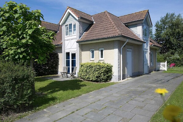 A two-story house with a paved driveway, a lawn, and a hedge. - Relaxing Villa by the Dunes (Kamperland)