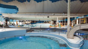 Una piscina interior con diseño curvo, una zona cubierta con decoración azul y blanca y un tobogán.