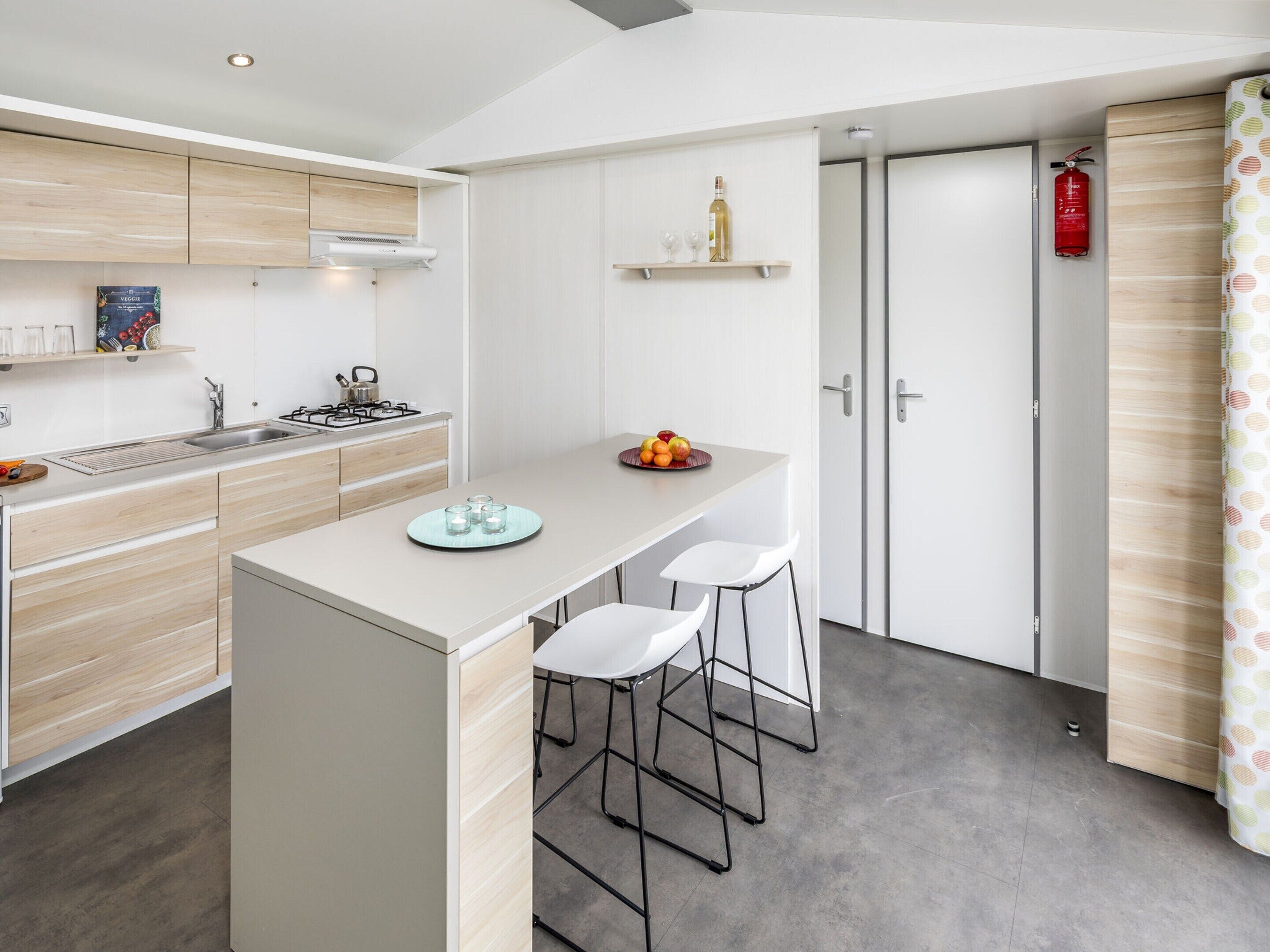 A modern kitchen with a central island, bar stools, a built-in stove, and a wine bottle on a shelf.