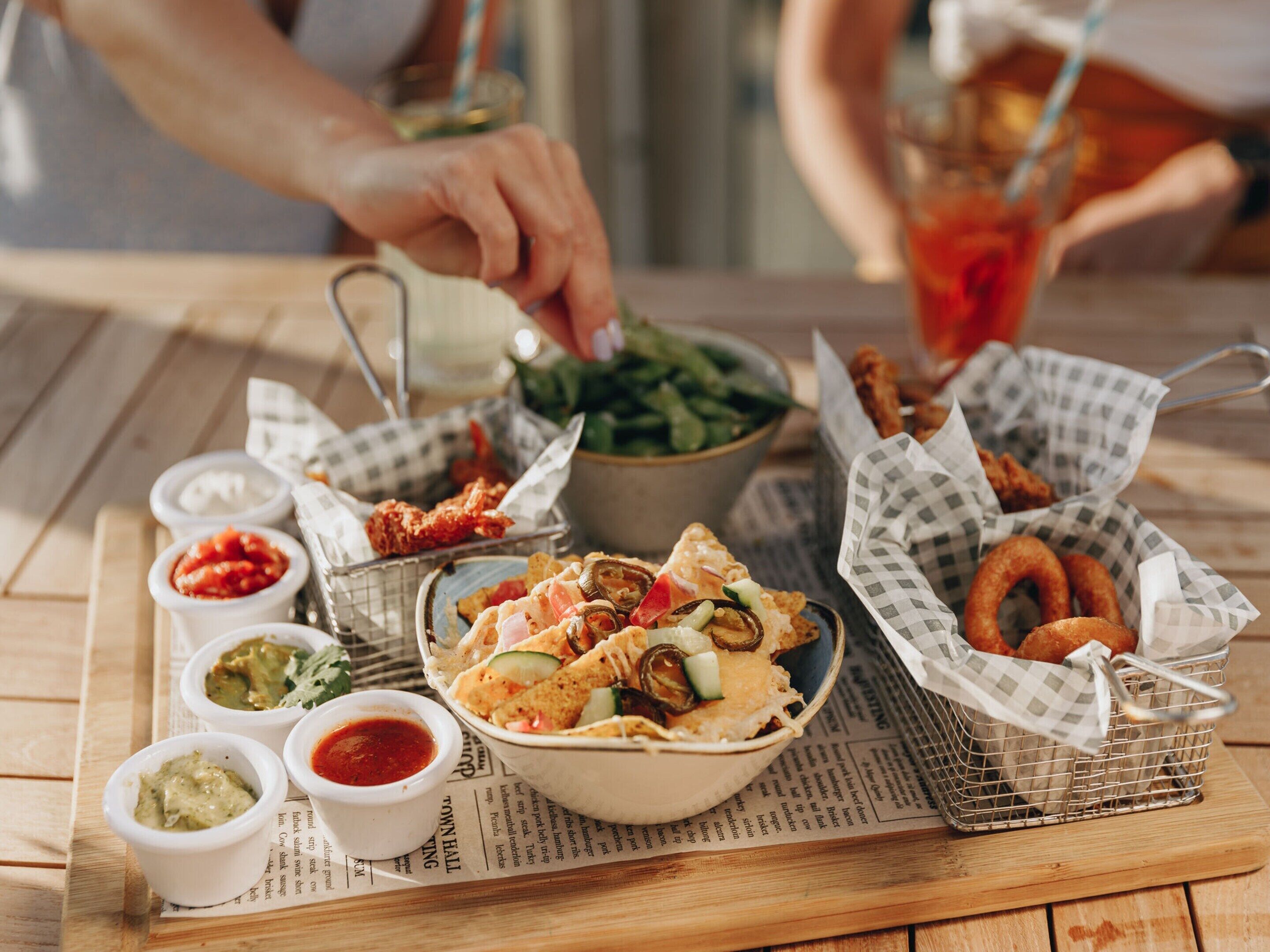 A wooden table with various food items including nachos, fried chicken, and onion rings, accompanied by small bowls of sauces.