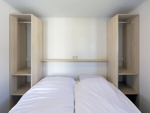 A bedroom with a bed, two wooden shelves, and a power outlet on the wall. - Chalet in Kamperland Near the Beach (Kamperland)
