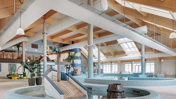 Un'ampia area piscina coperta con scivolo, diverse zone relax e un elemento d'acqua centrale.