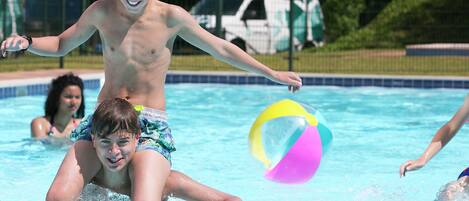 A swimming pool with clear blue water, a child playing with a ball, and a white van in the background.