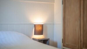 Una cama bien hecha con una lámpara de noche, un armario de madera y una pared blanca.