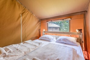 A single bed with white linens and pillows, a window with a view of greenery, and a lamp on the nightstand.