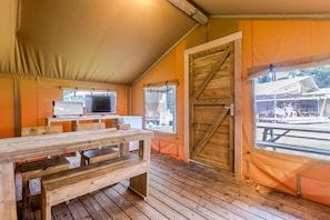 A tented room with wooden benches, a television, and a large wooden door.