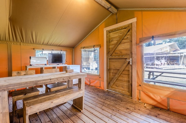 A tented room with wooden benches, a television, and a large wooden door.