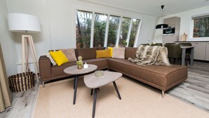 A modern living room with a sectional sofa, a round coffee table, and a dining area with a kitchen in the background. - Modern Villa Near Veluwe (Hoenderloo)