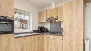A modern kitchen with wooden cabinets, a built-in oven, a coffee maker, and a stove. - Chic Chalet Near Almelo (Hoge Hexel)