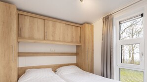 A bedroom with a wooden headboard, a bed with white bedding, a window with curtains, and a view of trees. - Chic Chalet Near Almelo (Hoge Hexel)
