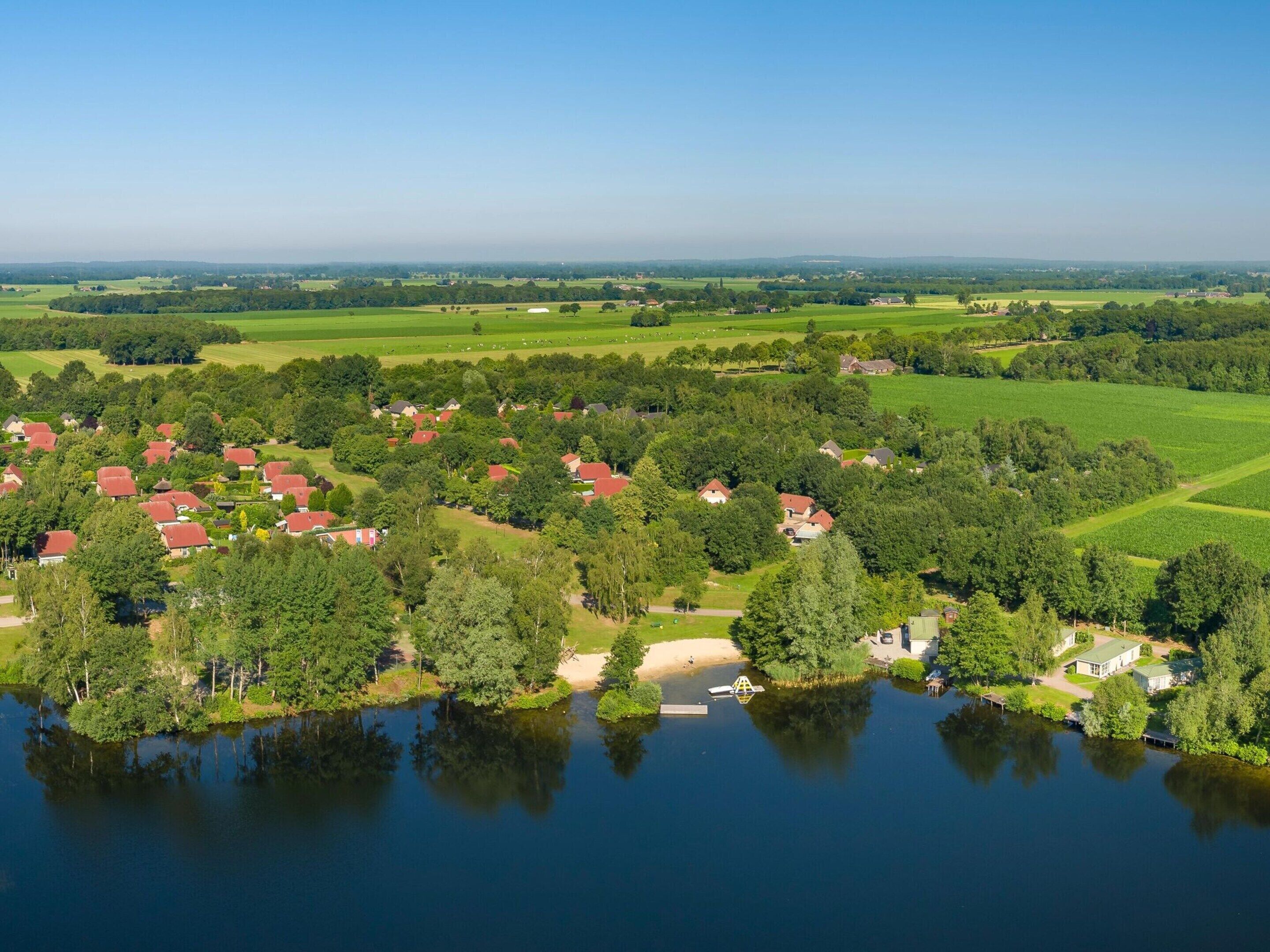 An aerial view of a lakeside residential area with houses surrounded by greenery and fields.