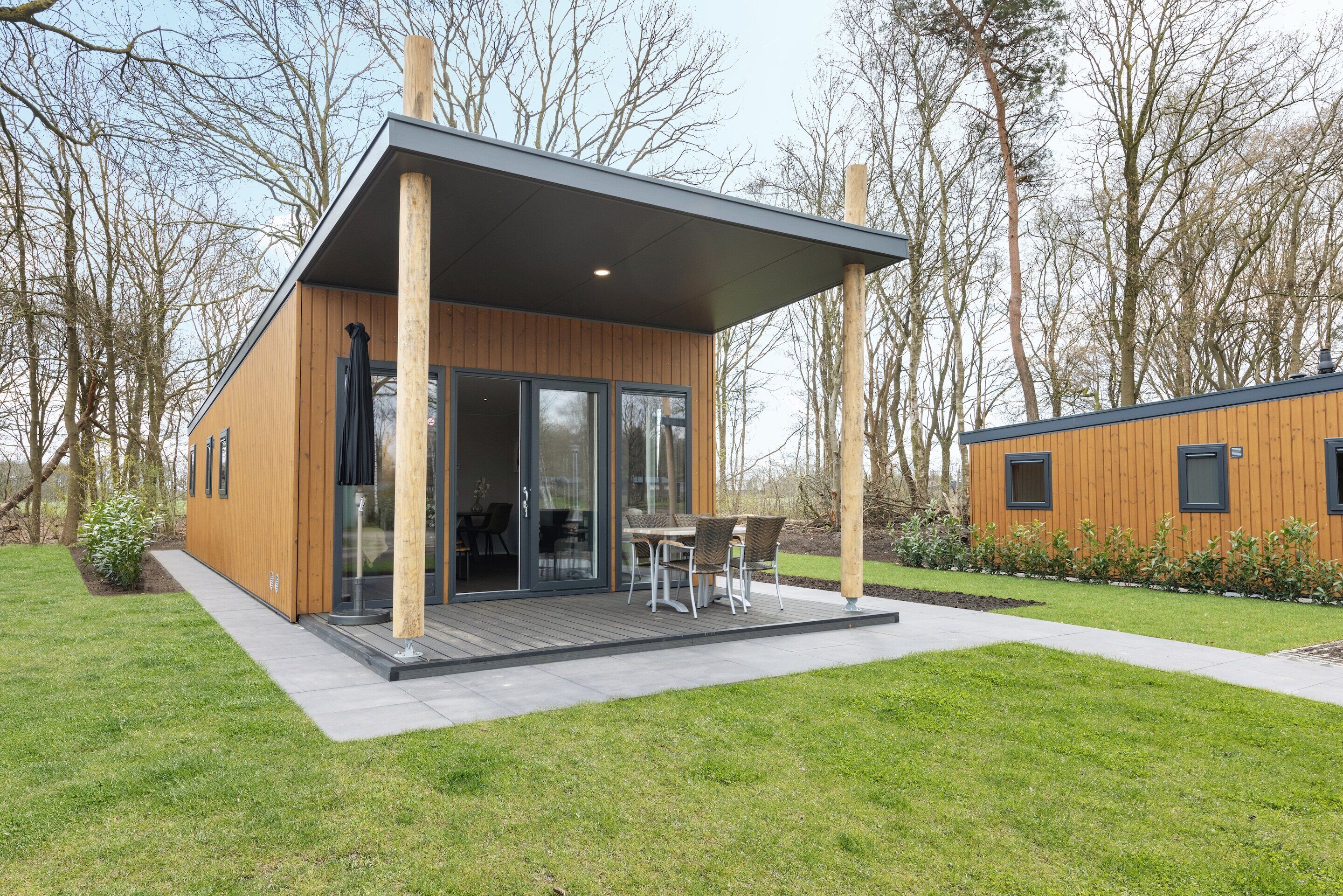 Un'accogliente baita in legno dal design moderno, con ingresso tramite porta in vetro, un patio con tavolo e sedie e un piccolo giardino.
