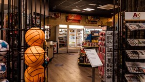 En butiksinredning med en skylt som säger ”Välkommen”, hyllor fyllda med olika produkter och en utställning med sportbollar.