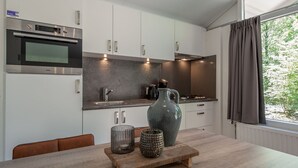 Ett modernt kök med vita skåp, rostfria vitvaror och ett stort fönster med gardiner.