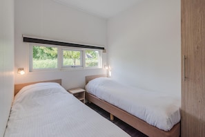 A room with two single beds, a window with a view of greenery, and a nightstand with a lamp. - Cozy Chalet With Sloop in Giethoorn (Giethoorn)