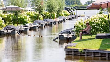 A riverside setting with boats docked, a person fishing, and a bridge in the background.