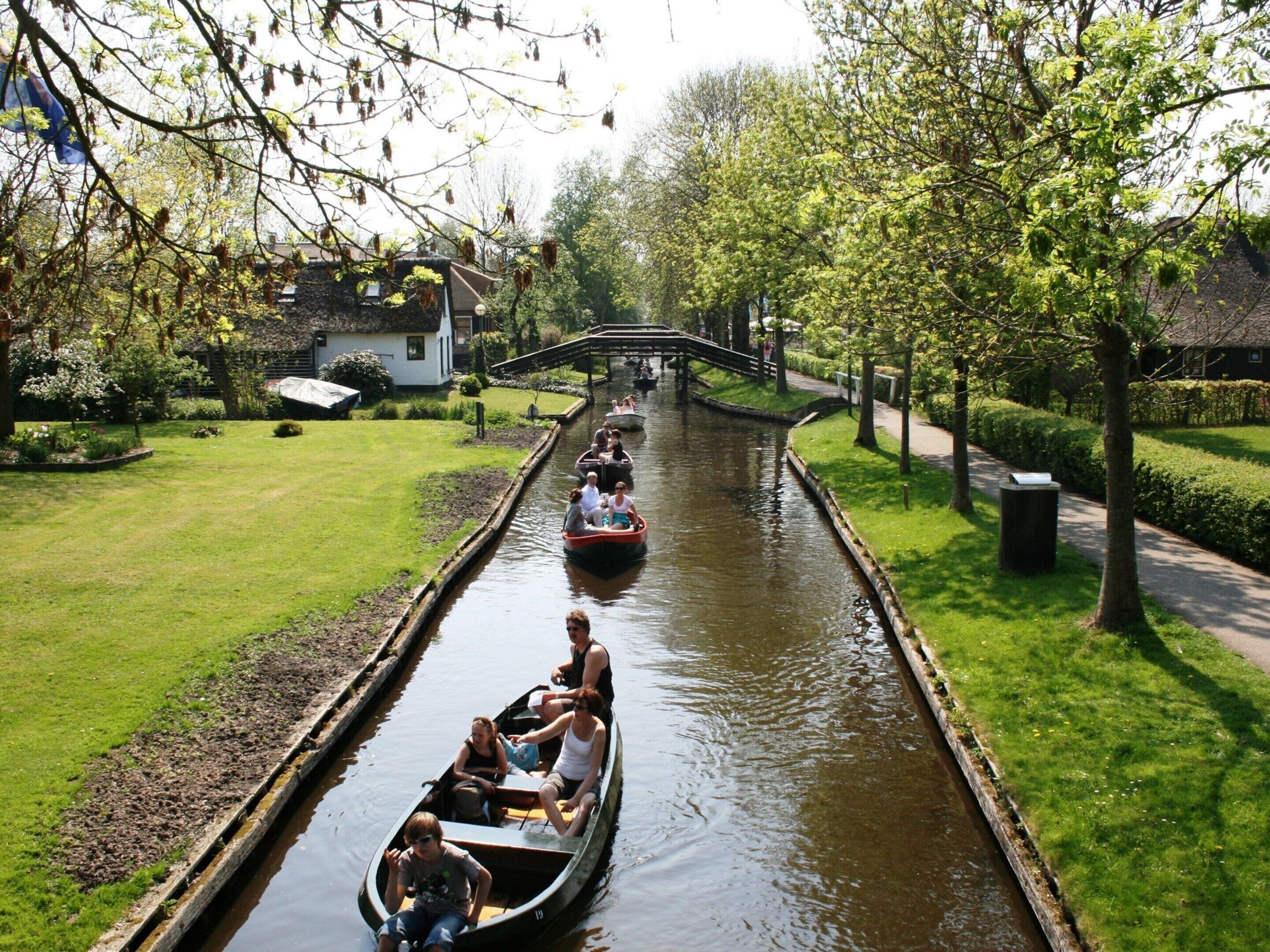 Ein Kanal mit Booten, einer Brücke und einem von Bäumen gesäumten Weg.