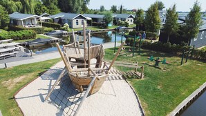 A playground with a wooden ship structure, a sandy play area, and a water body. - Cozy Chalet With Sloop in Giethoorn (Giethoorn)
