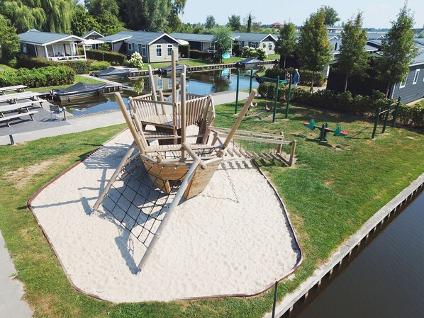 A playground with a wooden ship structure, a sandy play area, and a water body. - Cozy Chalet With Sloop in Giethoorn (Giethoorn)