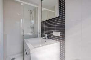 A modern bathroom with a glass shower enclosure, a white sink, and black tiled walls. - Cozy Chalet With Sloop in Giethoorn (Giethoorn)