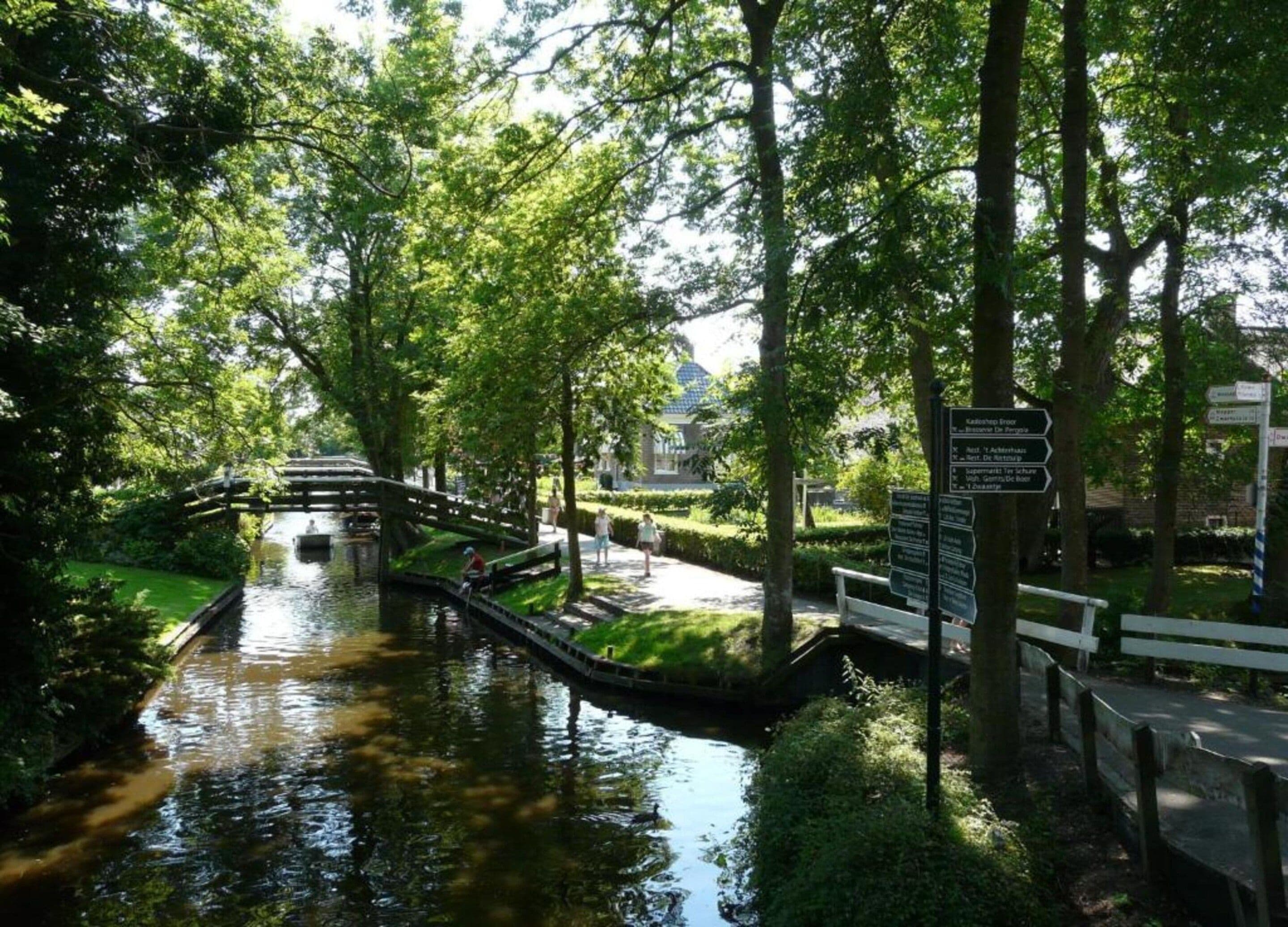 Un canal tranquilo con un puente de madera, rodeado de abundante follaje y árboles.