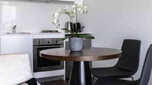 Una cocina moderna con armarios blancos, una mesa redonda de madera con una orquídea en maceta y sillas negras.