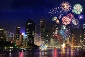 A city skyline at night with illuminated buildings and fireworks in the sky.