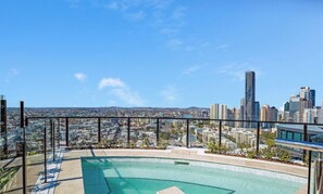 A rooftop pool with a cityscape view, glass railings, and a clear sky.