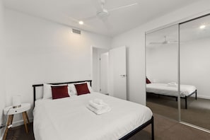 Et moderne hotelværelse med en stor seng, et sengebord med lampe, en loftsvifte og et stort spejl.