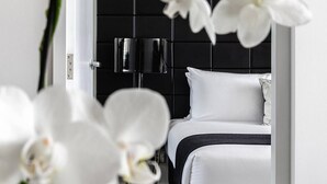 Un dormitorio moderno con cabecera negra, ropa de cama blanca y una lámpara de noche.