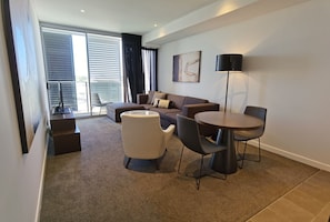 A modern living room with a sofa, a round table, and a coffee table. There is a sliding glass door leading to a balcony.