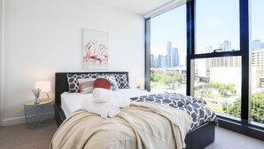 Une chambre d’hôtel moderne dotée d’une grande fenêtre, d’un lit avec une literie à motifs, d’une table de chevet avec une lampe et offrant une vue sur la ville.