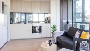 A modern kitchen with white cabinets, stainless steel appliances, and a large window. - KOZYGURU | DOCKLANDS | HIGH LEVEL WATERVIEW | 1BED  |  POOL  | VDO883 (Docklands)