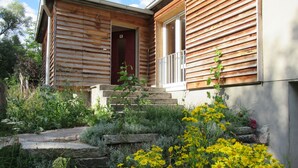 Una casa de madera con puerta roja, escalones de piedra y un jardín con flores amarillas.